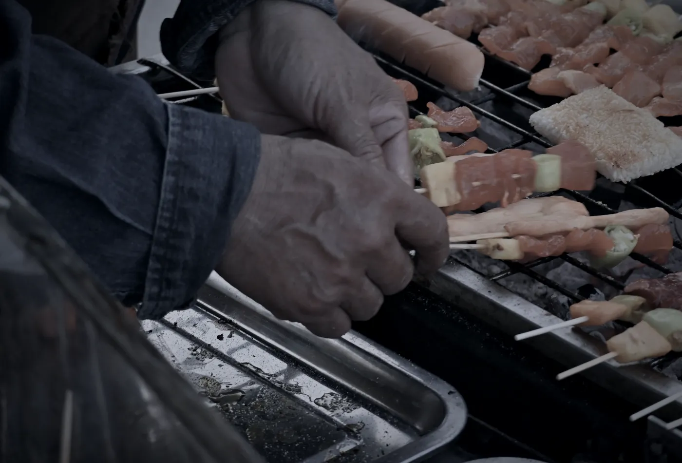 Unas manos trabajando la parrilla de La Cuadra, con la bandeja del pase al lado (foto de muestra)