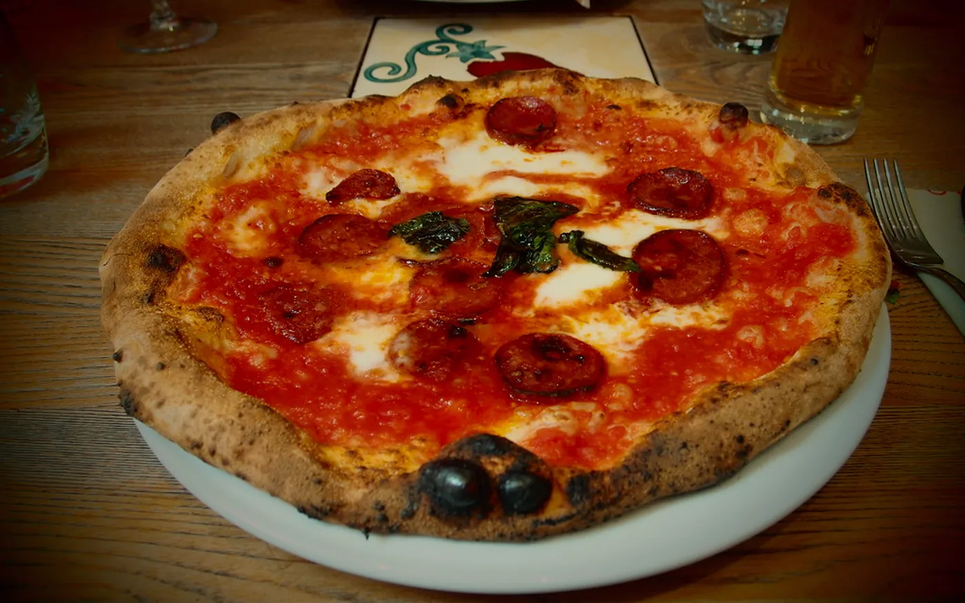 Pizza de la casa recién salida del horno, con pepperoni y chorizo, sobre fondo oscuro